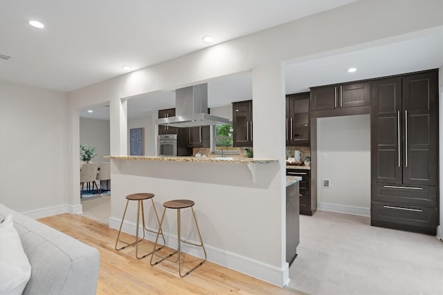 6405 Danwood Dr, Austin, TX 78759 - kitchen featuring range hood, stainless steel oven, a kitchen bar, light stone countertops, and recessed lighting