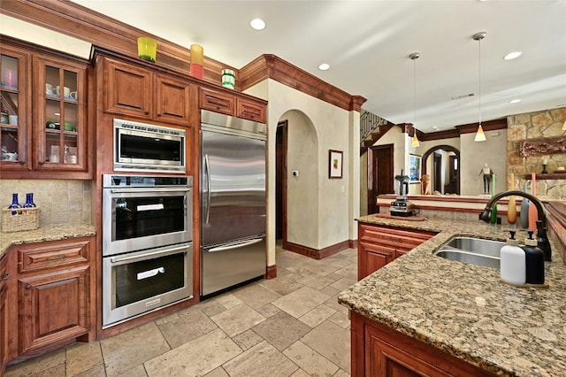 3111 Ski Shores Ter, Austin, TX 78730 - kitchen featuring built in appliances, arched walkways, stone tile flooring, decorative light fixtures, and tasteful backsplash