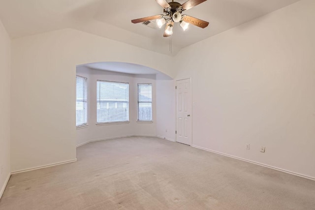 empty room featuring arched walkways, ceiling fan, light colored carpet, and baseboards