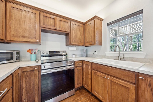 kitchen featuring appliances with stainless steel finishes, brown cabinets, light countertops, and a sink