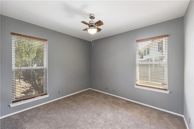 carpeted empty room featuring a ceiling fan, a wealth of natural light, and baseboards