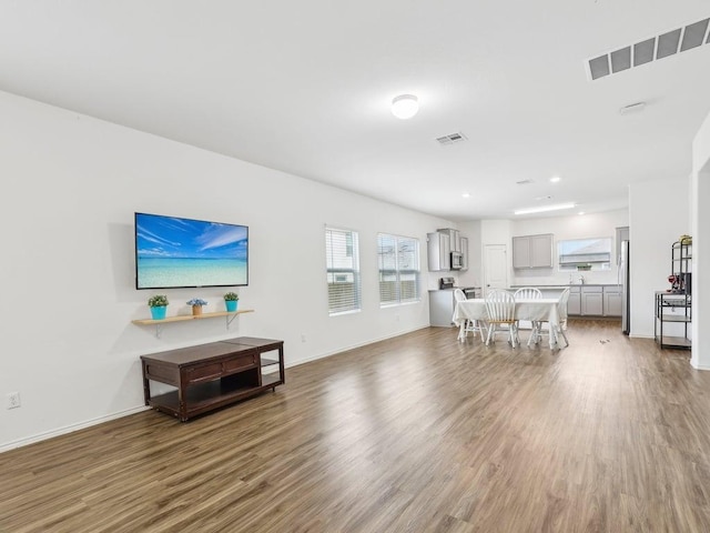 living area with visible vents, baseboards, wood finished floors, and plenty of natural light