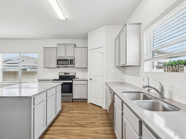 kitchen featuring a sink, stainless steel appliances, tasteful backsplash, light wood-style flooring, and light countertops