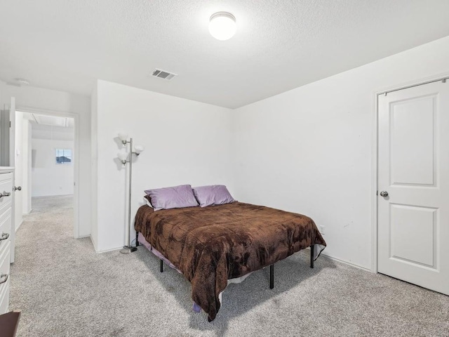 bedroom featuring attic access, a textured ceiling, visible vents, and light colored carpet