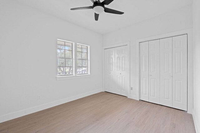 unfurnished bedroom with wood finished floors, a ceiling fan, baseboards, and two closets
