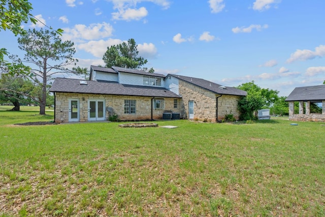 rear view of house with a yard, roof with shingles, stone siding, and central air condition unit