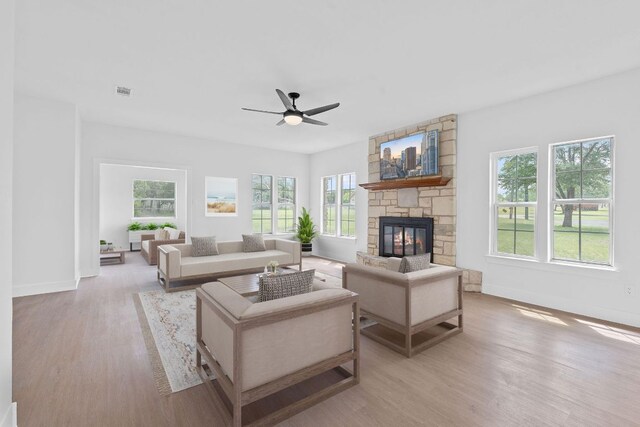 living area featuring ceiling fan, a stone fireplace, baseboards, wood finished floors, and visible vents
