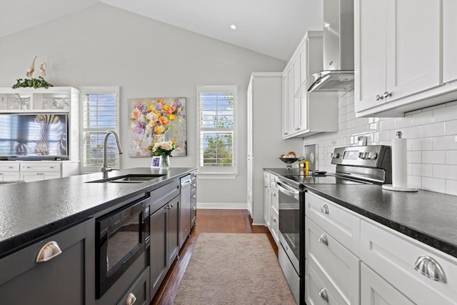 kitchen featuring wall chimney range hood, a sink, appliances with stainless steel finishes, dark countertops, and vaulted ceiling