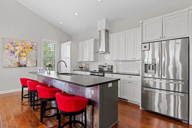 kitchen with an island with sink, stainless steel appliances, backsplash, a sink, and wall chimney exhaust hood