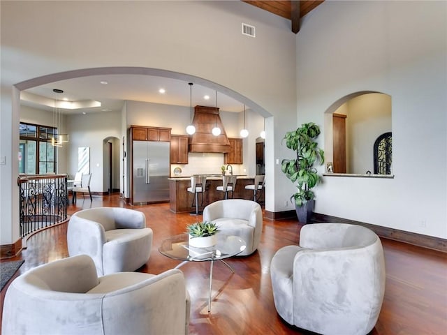 living area featuring visible vents, baseboards, arched walkways, dark wood-style flooring, and a towering ceiling