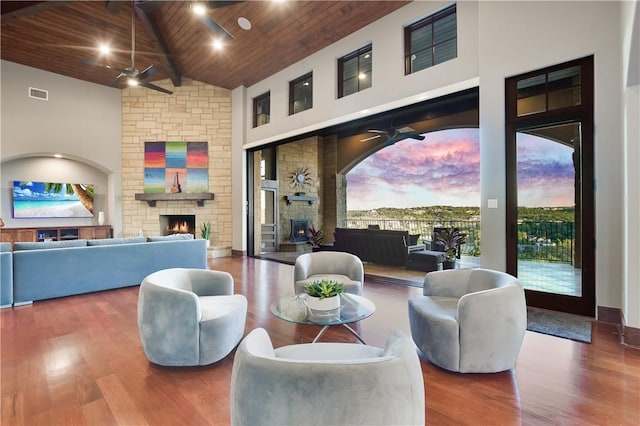 interior space with a ceiling fan, a stone fireplace, wooden ceiling, and visible vents