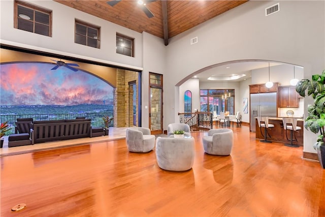 living room with visible vents, wooden ceiling, a towering ceiling, wood finished floors, and ceiling fan with notable chandelier