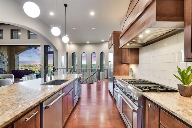 kitchen with a sink, stainless steel appliances, wall chimney exhaust hood, light stone counters, and plenty of natural light