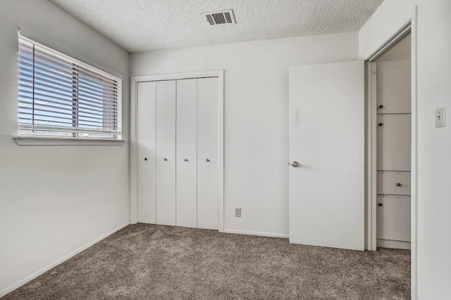 unfurnished bedroom with visible vents, a textured ceiling, a closet, and carpet