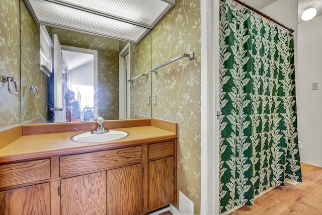 bathroom with wood finished floors, vanity, visible vents, and wallpapered walls