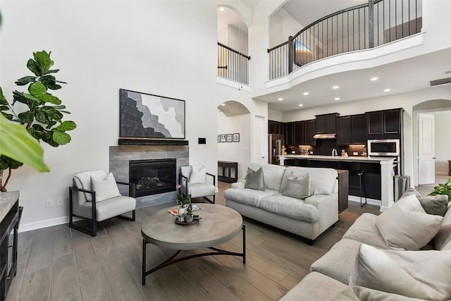 361 Wild Pecan Loop, Buda, TX 78610 - living area featuring arched walkways, dark wood-type flooring, a tile fireplace, a high ceiling, and recessed lighting