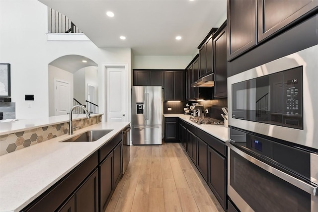 361 Wild Pecan Loop, Buda, TX 78610 - kitchen featuring stainless steel appliances, decorative backsplash, under cabinet range hood, arched walkways, and light wood-type flooring