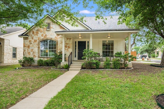 view of front facade featuring a porch, a front lawn, roof with shingles, and stone siding