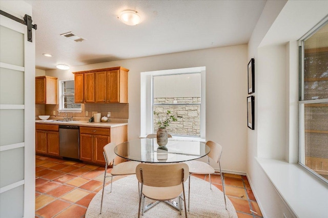 kitchen with light tile patterned flooring, visible vents, backsplash, light countertops, and stainless steel dishwasher