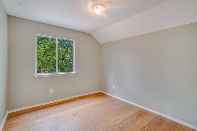additional living space featuring baseboards, light wood finished floors, and vaulted ceiling