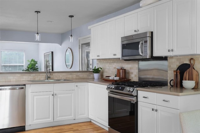 5707 Ave G, Austin, TX 78752 - kitchen featuring appliances with stainless steel finishes, a sink, decorative backsplash, light wood finished floors, and decorative light fixtures