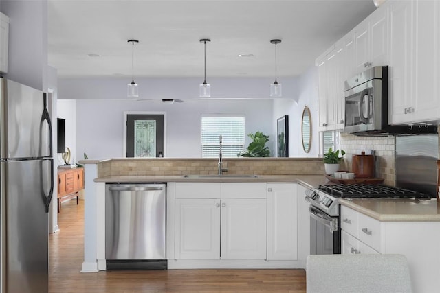 5707 Ave G, Austin, TX 78752 - kitchen with stainless steel appliances, a sink, backsplash, light wood-style floors, and a peninsula