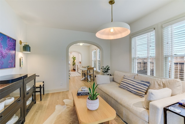 living area featuring light wood finished floors, arched walkways, and baseboards