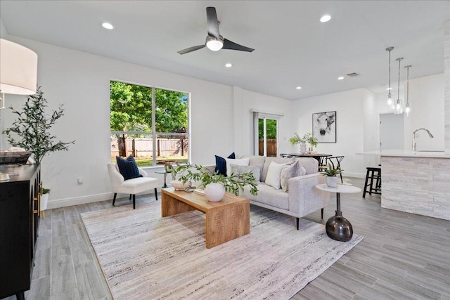 living area featuring light wood-style floors, visible vents, baseboards, recessed lighting, and a ceiling fan
