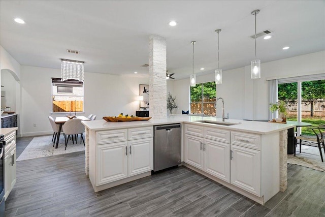 kitchen with light countertops, a peninsula, stainless steel dishwasher, and a sink