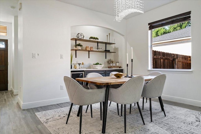 dining area featuring beverage cooler, an inviting chandelier, light wood-style flooring, and baseboards