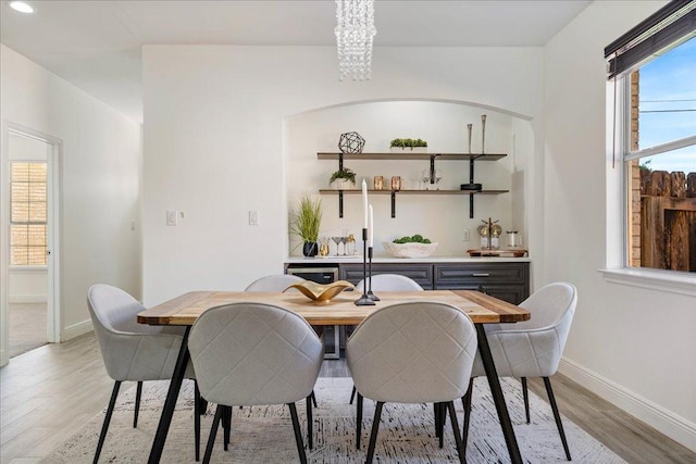dining room with light wood-style floors, a notable chandelier, wet bar, and baseboards