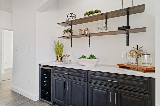 bar with light wood-style floors, wine cooler, bar, baseboards, and arched walkways