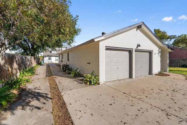 view of side of property with fence, a detached garage, and brick siding
