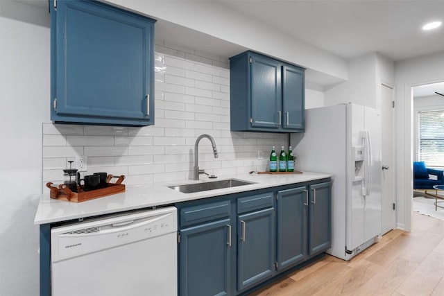 kitchen with tasteful backsplash, a sink, light countertops, blue cabinets, and white appliances