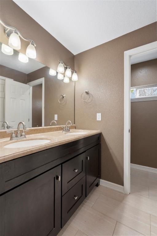 full bath with baseboards, tile patterned flooring, double vanity, and a sink