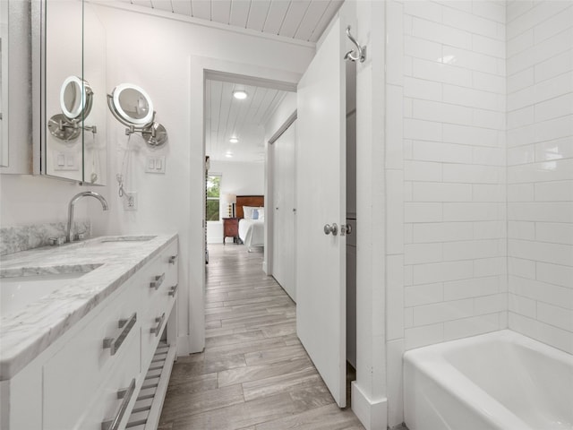 bathroom with recessed lighting, wood finished floors, double vanity, ensuite bathroom, and a sink