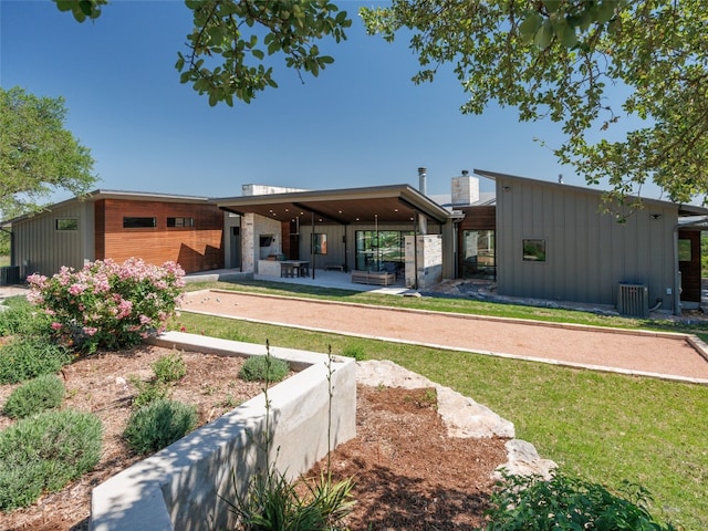back of property with board and batten siding, central AC unit, a yard, and a patio area
