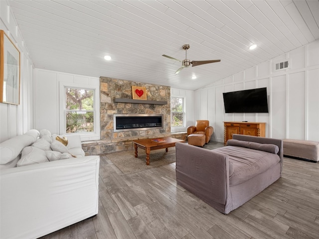 living area with lofted ceiling, visible vents, ceiling fan, wooden ceiling, and a decorative wall
