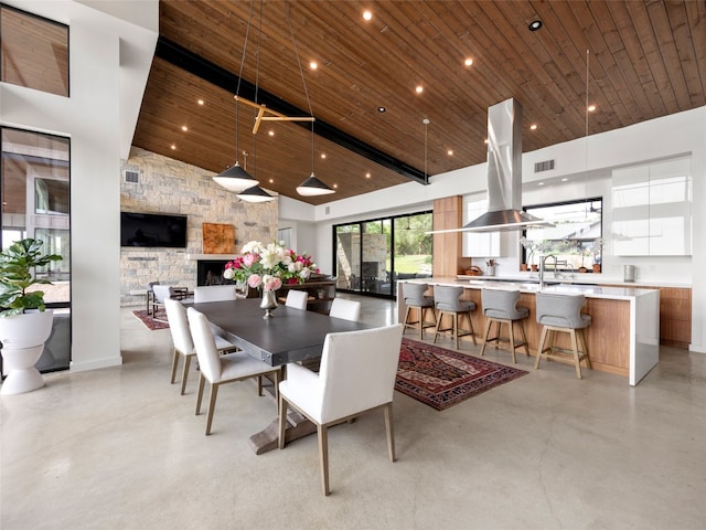 dining room with high vaulted ceiling, concrete flooring, a fireplace, and wood ceiling