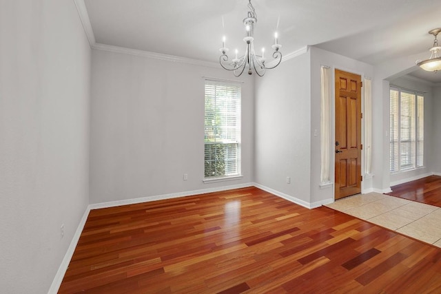 empty room featuring baseboards, ornamental molding, wood finished floors, and a notable chandelier