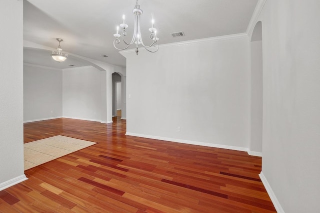 empty room with crown molding, arched walkways, wood finished floors, and visible vents