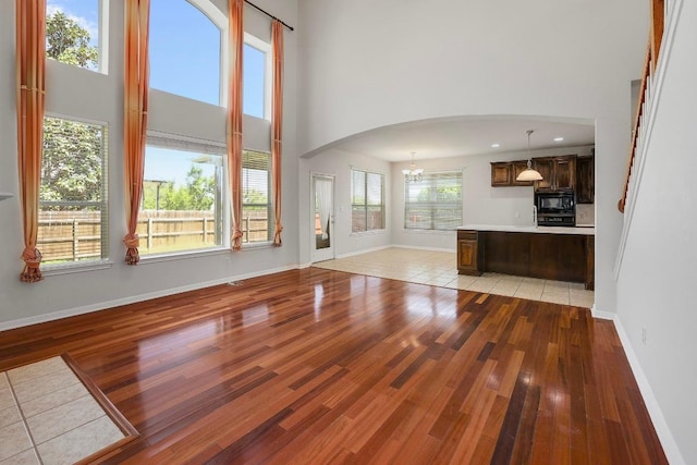 11100 Alison Parke Trl, Austin, TX 78750 - unfurnished living room with light wood-style floors, a high ceiling, a chandelier, baseboards, and arched walkways