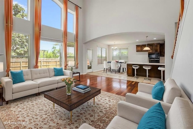 living area with arched walkways, a chandelier, light wood-style flooring, and a towering ceiling