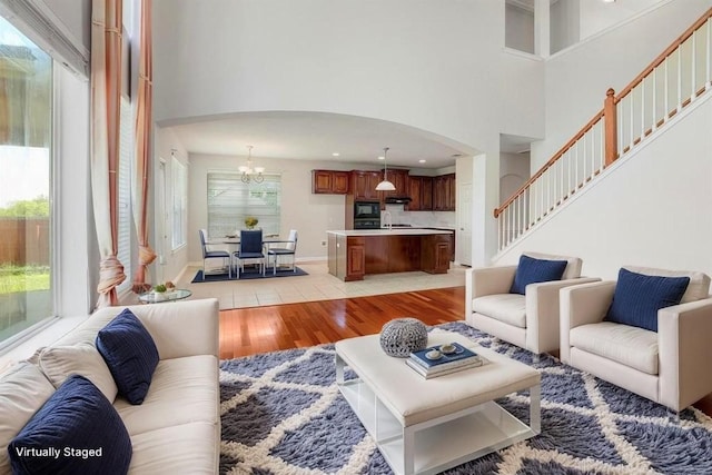 11100 Alison Parke Trl, Austin, TX 78750 - living room featuring arched walkways, light wood finished floors, a towering ceiling, a chandelier, and stairs