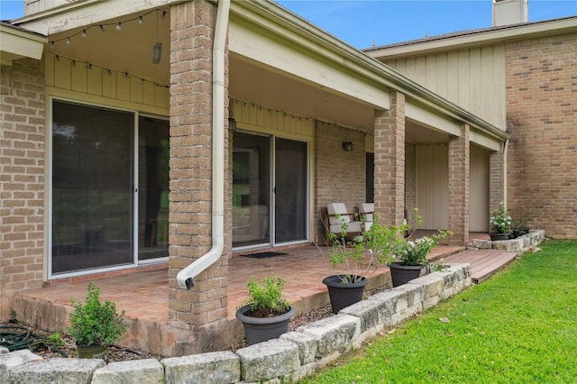 doorway to property with a chimney, brick siding, a yard, and a patio area