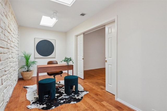 office space with baseboards, visible vents, a skylight, and wood finished floors
