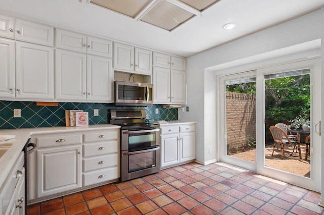 kitchen with tasteful backsplash, white cabinets, stainless steel appliances, light countertops, and baseboards