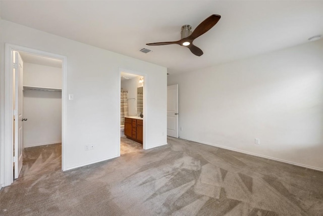 unfurnished bedroom featuring a closet, a walk in closet, light colored carpet, and visible vents