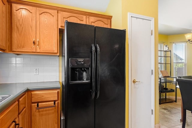 kitchen featuring brown cabinetry, dark countertops, black refrigerator with ice dispenser, and decorative backsplash