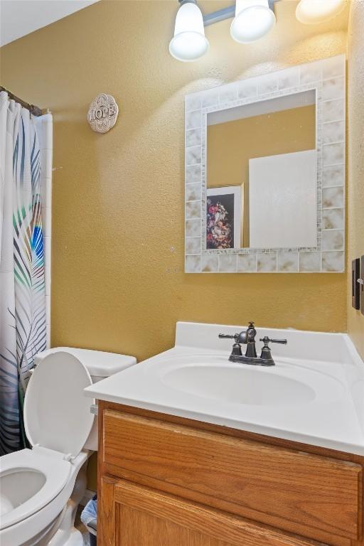 full bathroom featuring toilet, a textured wall, vanity, and a shower with curtain